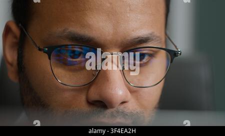 Close up focused Indian male business man in eyeglasses looking laptop screen concentrated businessman programming coding at night computer light Stock Photo