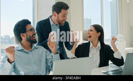 Happy multiethnic business team work laptop celebrating success inside office sales win corporate teamwork excited smiling businessmen businesswoman Stock Photo