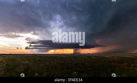 View of a dramatic supercell thunderstorm with dark, swirling clouds and rain curtains over the flat plains during sunset in Oklahoma City, Oklahoma, Stock Photo