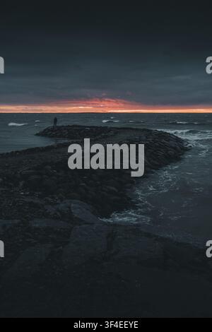 View of Saxby rannik with a person standing on the stone breakwater during a dramatic sunset over the sea in Saxby, Laane maakond, Estonia. Stock Photo