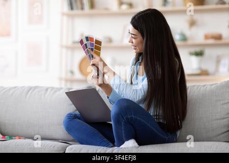 Online Design Courses. Asian Woman Holding Colour Swatch And Using Laptop At Home Stock Photo