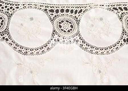 Detail of a crocheted and cross-stitched tablecloth on a black background, border decoration. Crafts, vintage linens. Hobby concept. Top view. Natural Stock Photo