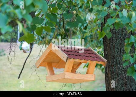 Bird feeder in the form of a birdhouse on a background of green leaves Stock Photo