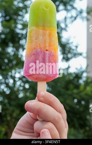 Fruit ice cream in a child's hand on a nature background. Multicolored ice cream. Stock Photo