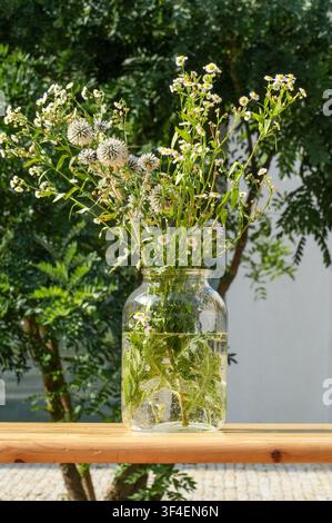 A bouquet of wildflowers in a glass vase on a table in the park. Stock Photo