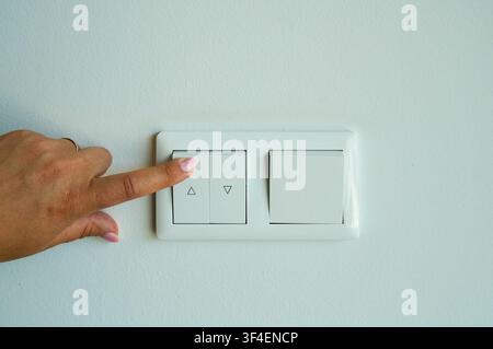 Close up of woman hand turning on light switch on white wall Stock Photo