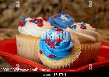 Delicious cupcakes with blue, white, and red frosting. Red stars decorate the swirls with festive flair. Cupcakes rest on a vibrant red plate. Backgro Stock Photo