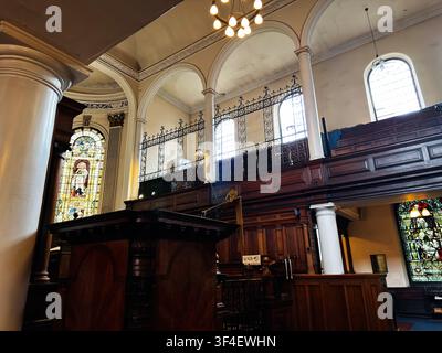 Manchester, UK - May 10, 2026: Ornate wooden pulpit and gallery framed by columns and colorful stained glass in a Manchester St Ann's church. Stock Photo