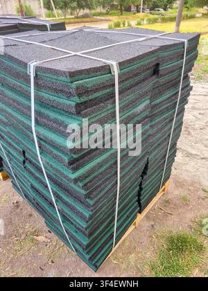 A large stack of durable rubber tiles, commonly used for playgrounds and safety surfaces, is secured with straps on a wooden pallet Stock Photo