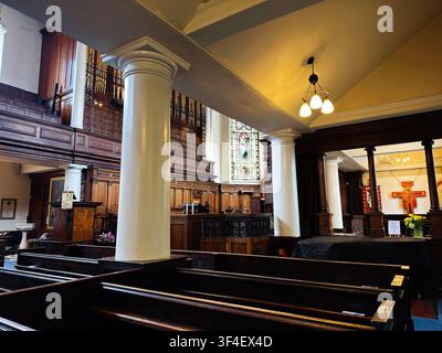 Manchester, UK - May 10, 2026: Calm, traditional St Ann's church interior featuring wooden pews, white columns, stained glass, and warm lighting. Stock Photo