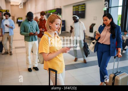 People waiting in line at airport terminal using smartphones Stock Photo