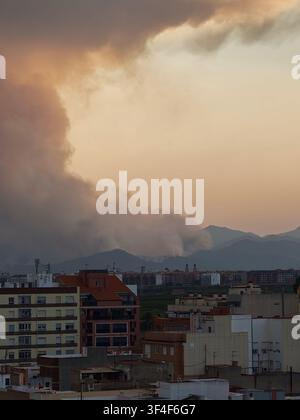 City buildings overlooking distant mountains with a large plume of smoke rising from a wildfire, creating a hazy atmosphere over almassora, valencian Stock Photo