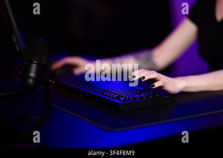 Young woman using keyboard and microphone in dark gaming setup Stock Photo