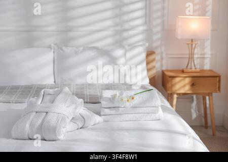 Clean bathrobes with flowers and towels on bed indoors Stock Photo