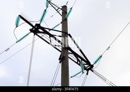 High-voltage power lines, view from below. Concrete top of a transmission tower with metal cross beams and fiberglass pin insulators. Industrial lands Stock Photo