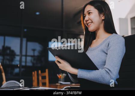 young woman is working on laptop in modern office environment, showcasing focused and productive atmosphere. She is dressed in professional white shir Stock Photo