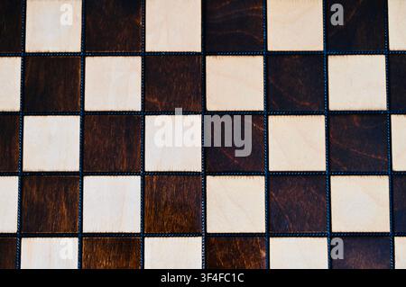A clean, top-down flat lay photograph of an empty wooden chessboard showing alternating light and dark squares with natural wood grain texture. The minimalistic pattern serves as a versatile background or template for strategic concepts, business planning, decision-making framework, game design, and intellectual themes. Perfect space for placing custom text or objects. Stock Photo