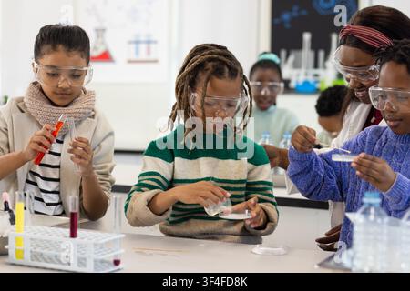 African teenage students and teacher in labcoat conducting experiment at bench petri dish goggles Stock Photo