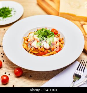 Seafood pasta with shrimps, mussels, cherry tomatoes and fresh arugula in a white plate on a wooden table with parmesan and parsley. Stock Photo