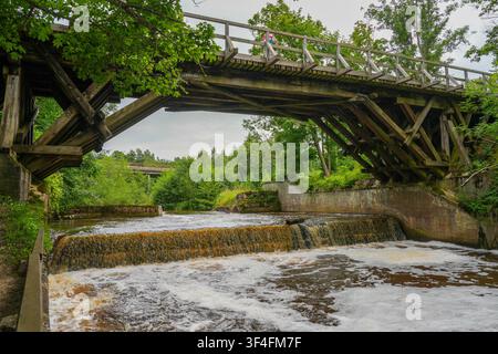 Historic Wooden Bridge Over Riva River with Small Waterfall in Latvia's Scenic Countryside Landscape Stock Photo