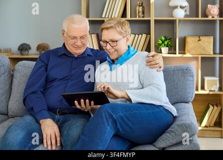 Smiling senior couple using digital tablet together at home on a comfortable couch Stock Photo