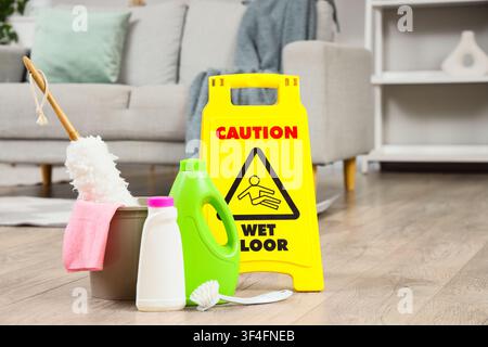 Cleaning supplies and a yellow caution wet floor sign on a wooden floor in a modern living room, Cleaning supplies including bottles of detergent, a b Stock Photo