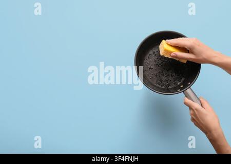 Womans hands cleaning a dirty frying pan with a yellow sponge, kitchen chores and domestic work Stock Photo