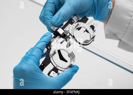 Optometrist hands in blue gloves holding a trial frame for vision testing and eye examination, the detailed close-up highlights the precision and care Stock Photo