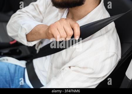 Man fastening a black seat belt in a car, road safety and responsible driving concept, close up view Stock Photo