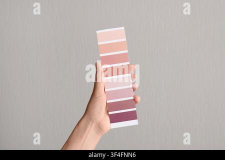 Hand holding a color palette with various shades of pink and purple against a neutral background Stock Photo