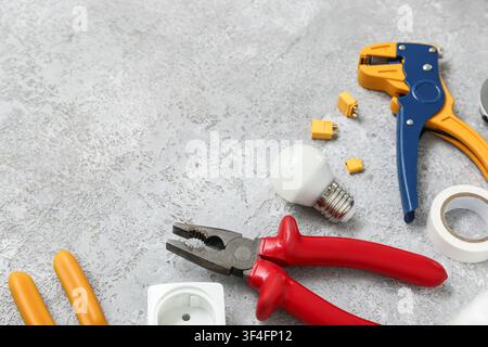 Electricians tools, light bulb and electric socket on grey grunge background Stock Photo