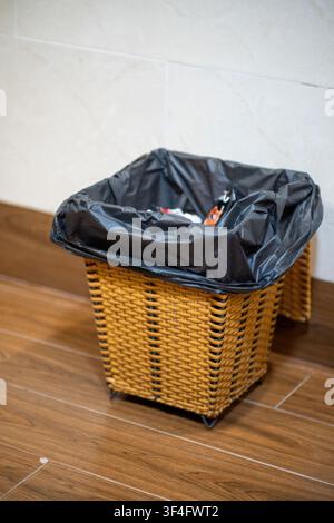 Wicker trash bin with black liner on wooden floor Stock Photo