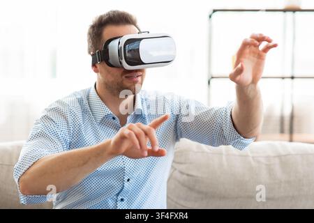 Young guy wearing virtual reality glasses, sitting on sofa Stock Photo