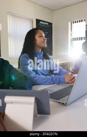 Teen girl pupil sitting at desk in class wearing light-blue top looking right using laptop tablet Stock Photo