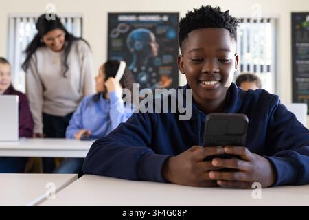Diverse teen class working at desks with laptops, teen in navy hoodie using handheld device Stock Photo