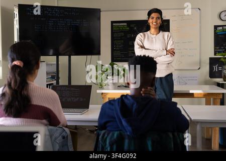 Indian woman instructor presenting to teenage students in classroom, monitor and laptop with code Stock Photo