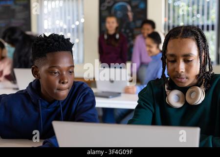 Two African American teenage male students sharing laptop and headphones collaborating in classroom Stock Photo