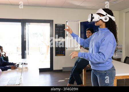 Teen classmates watching student wearing white VR headset gesturing in lab with laptop, copy space Stock Photo