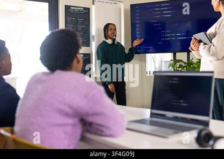 Diverse female students watching African American teen presenting code in classroom with monitor Stock Photo