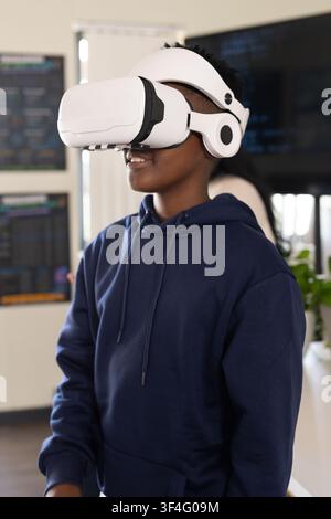 African American youth male wearing navy hoodie testing VR headset in tech lab with code monitors Stock Photo