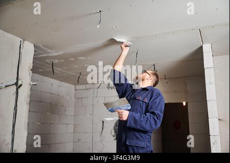Worker patching overhead joint with filler in room under construction. Building workflow, restoration process, home renovation and structural improvement concept Stock Photo