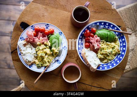 Healthy breakfast with scrambled eggs, avocado, prosciutto, cherry tomatoes and bread on rustic wooden table, served with coffee, balanced meal and clean eating lifestyle concept Stock Photo