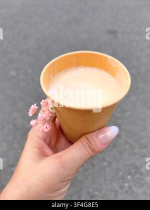 Womans hand holding a paper cup of coffee with small pink flowers Stock Photo