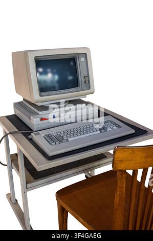Vintage desktop computer setup from the 1980s with CRT monitor, mechanical keyboard, horizontal case, and wooden chair isolated on a white background. Stock Photo