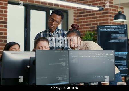 Developers Brainstorming Code Feedback with Intern in a software development office, showing programmers collaborating on source code, algorithms and data coding workflow. Stock Photo