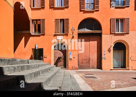 Bologna, Italy - May 2026: Historic orange terracotta building facade with arched wooden portal and stone public steps Stock Photo