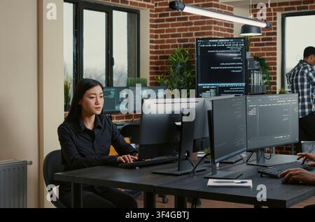 Programmer holding a clipboard sits near a colleague writing code as database admins work on big data, machine learning software and a shared development project. Stock Photo
