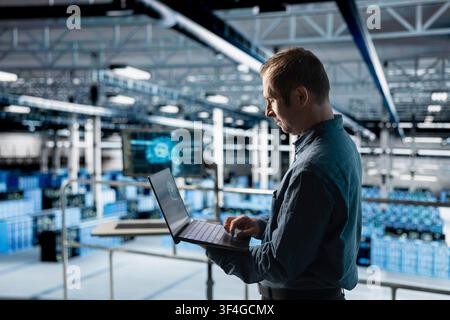Data center programmer using laptop to review code for AI enhanced automation scripts. Employee in server farm running AI assisted diagnostics on infrastructure for predictive fault detection Stock Photo