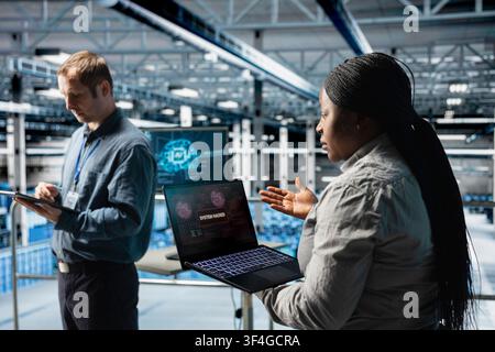 Server farm coworkers stressed by hacking attempts on systems, using AI to fix problems. Team of data center technicians scanning for vulnerabilities in firewall using artificial intelligence Stock Photo