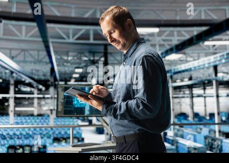 System administrator using tablet in in data center maintaining infrastructure for AI workloads. IT professional in server farm utilizing high tech server clusters for parallel AI processing Stock Photo